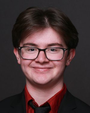 Portrait of Alexander Munson in a black suit jacket, red shirt, and black tie.